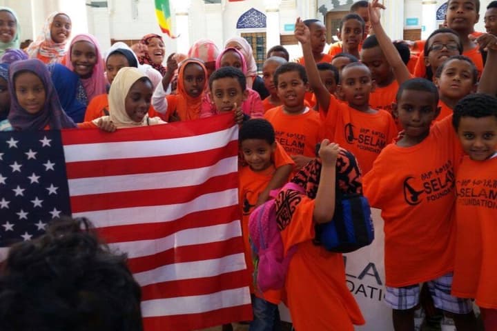 Selam Youth gather outdoors for a community group photo with Selam Foundation shirts and flags